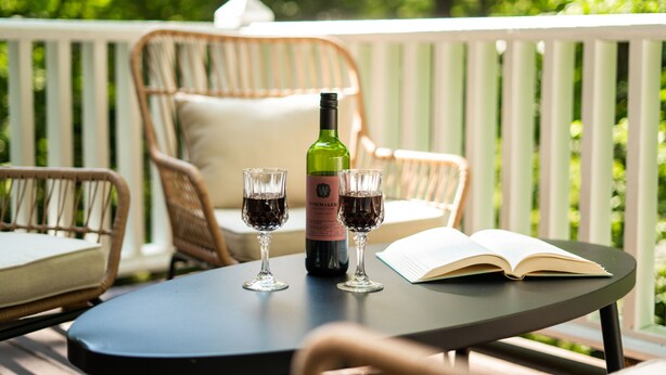 A table with a bottle and two glasses on a deck with wicker chairs and a white railing. - Riverview Retreat at The Wanderer  (Boone)