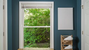 A room with teal walls, a large window with a view of greenery, a bench with a fur throw, a wicker chair with towels, and a white wall-mounted towel rack. - Riverview Retreat at The Wanderer  (Boone)