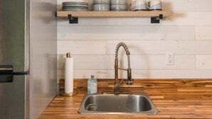 A kitchen with a stainless steel refrigerator, wooden countertop, and a sink with a faucet. There are shelves above the countertop holding dishes and glasses. - Riverview Retreat at The Wanderer  (Boone)