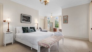 Une chambre spacieuse avec un grand lit, des lampes de chevet, un banc et un grand miroir.