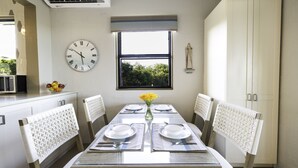 Un coin repas avec une table dressée pour quatre personnes, une horloge et une fenêtre donnant sur les arbres.