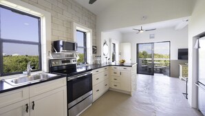 Une cuisine moderne avec des meubles blancs, des appareils en acier inoxydable et une grande fenêtre donnant sur un espace verdoyant.