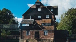 Un grand bâtiment en briques, à plusieurs étages, doté d’un toit à forte pente, situé près d’une étendue d’eau.