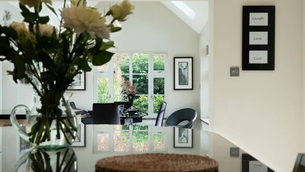 Un coin repas avec une table en verre, des chaises, un vase de fleurs et des tableaux encadrés accrochés au mur.