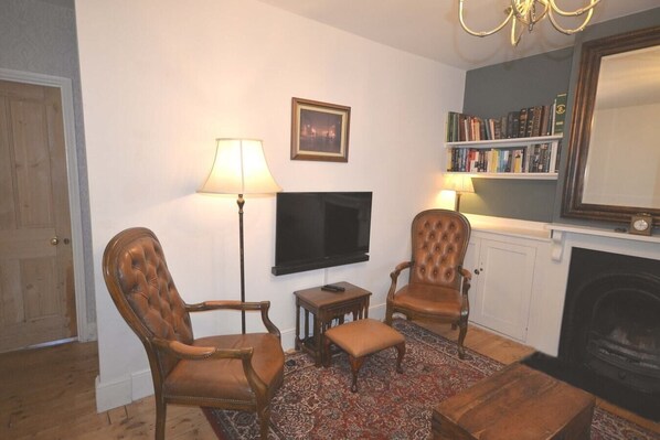 A living room with two leather armchairs, a small table, a television, a bookshelf, and a fireplace. - Delightful Cottage in Sandwich - One Bedroom (Kent)