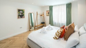 A hotel room with a large bed, a wooden bench, a mirror, and artwork on the walls. - 2Bed 2Bath Stunning Shoreditch Apartment (London)