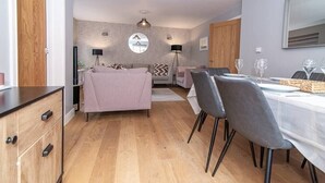 Una sala moderna con un sofá, una mesa de comedor y sillas. Se observa un aparador de madera y un espejo en la pared.