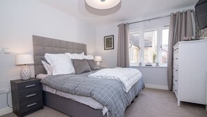 Un dormitorio con cama, mesitas de noche, cómoda y ventana con cortinas.