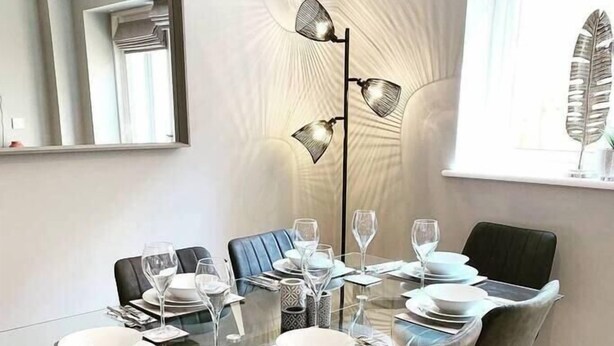 Un comedor moderno con una mesa de vidrio, sillas negras y una lámpara de pie.