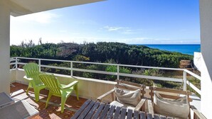 Un balcone con vista sull'oceano, una sedia verde e una panca di legno.