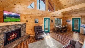 Ein gemütliches Blockhaus-Interieur mit Kamin aus Naturstein, Holzwänden, Essbereich und Küche.