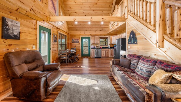 Ein Holzblockhaus-Interieur mit einer Wendeltreppe, einem Ledersessel, einer Couch mit gemusterten Kissen und einer Küchenzeile.
