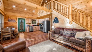 Ein Interieur einer Holzh ütte mit einer Holztreppe, einem Wohnzimmer mit einer Couch und einem Essbereich mit Tisch und Stühlen.