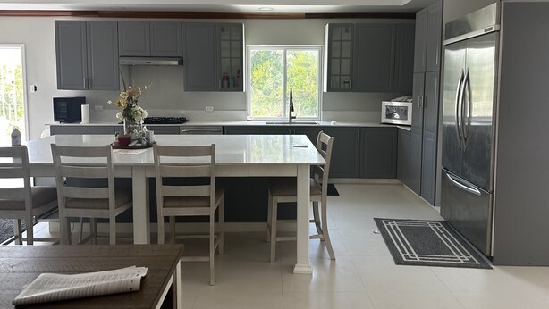 A modern kitchen with grey cabinets, a stainless steel refrigerator, and a dining area with white chairs and a table. - Bay Bliss Retreat home in Ironshore, Montego Bay, less than 10 mins to airport. (Montego Bay)