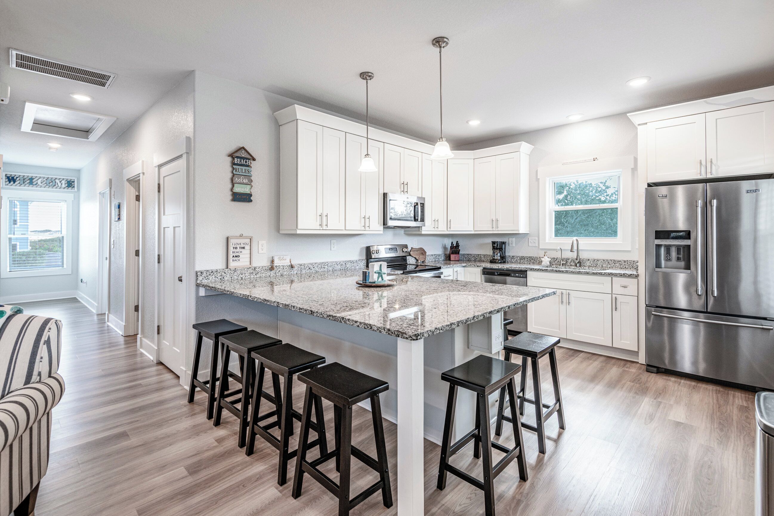 A modern kitchen with white cabinets, a large island with bar stools, stainless steel appliances, and pendant lighting.