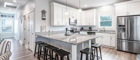 A modern kitchen with white cabinets, a large island with bar stools, stainless steel appliances, and pendant lighting.