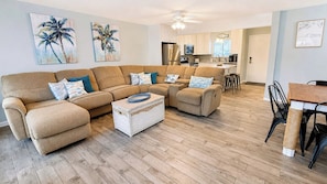 A living room with a sectional sofa, a coffee table, and a kitchen in the background. - Boat, Beach & Relax at SPC 3106 Canal-Front Condo + FREE Beach Service! (Destin)