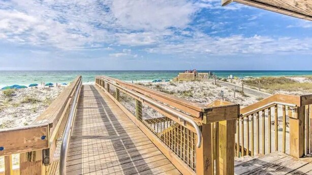 A wooden boardwalk leading to a beach with a clear view of the ocean and a sandy area with umbrellas. - Snowbird Retreat - Private Beach, Heated Pools, Pickleball & Golf! (Destin)