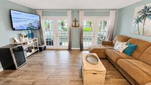 A living room with a TV, a sofa, a coffee table, and a bookshelf. - Snowbird Retreat - Private Beach, Heated Pools, Pickleball & Golf! (Destin)
