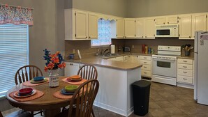 A kitchen with white cabinets, a central island, a chandelier, and a dining area with a table set for four. - Lake House on Weiss Lake! (Leesburg)