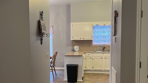 A kitchen with white cabinets, a countertop, and a window with a blue patterned view. - Lake House on Weiss Lake! (Leesburg)