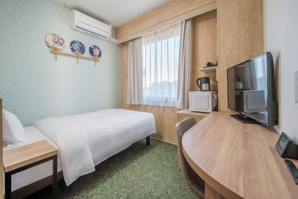 Una habitación de hotel con una cama, un escritorio con computadora, televisión y microondas.