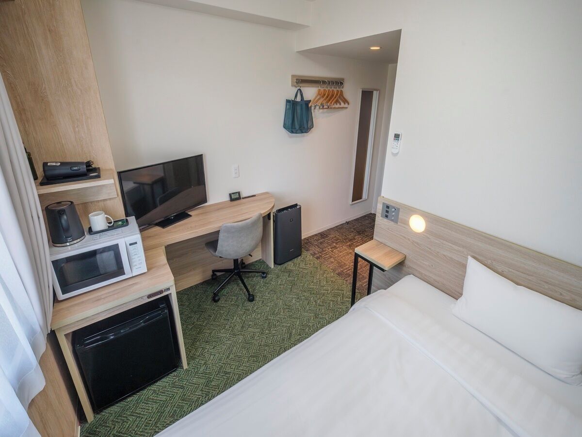 Ein kleines Hotelzimmer mit Bett, Schreibtisch, Mikrowelle, Kaffeemaschine und Fernseher.
