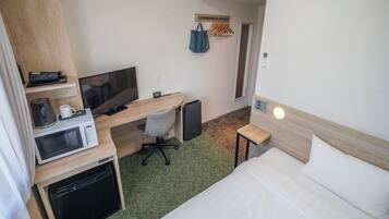 Ein kleines Hotelzimmer mit Bett, Schreibtisch, Mikrowelle, Kaffeemaschine und Fernseher.