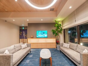 A modern living room with sofas, a coffee table, a TV, and a large window. - Tabino Hotel EXpress Narita (Narita)