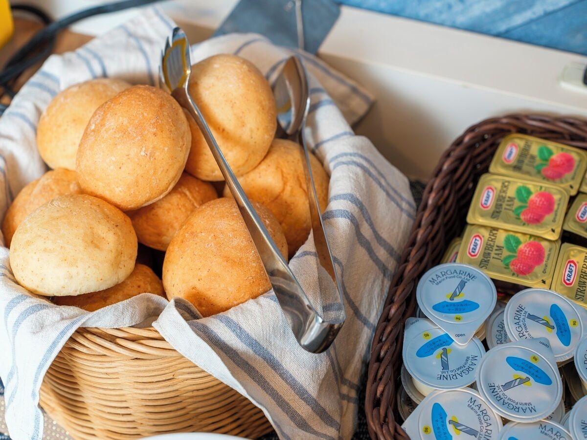 Ein Korb mit runden, goldbraunen Brötchen, einem gestreiften Tuch und Margarinegläsern.
