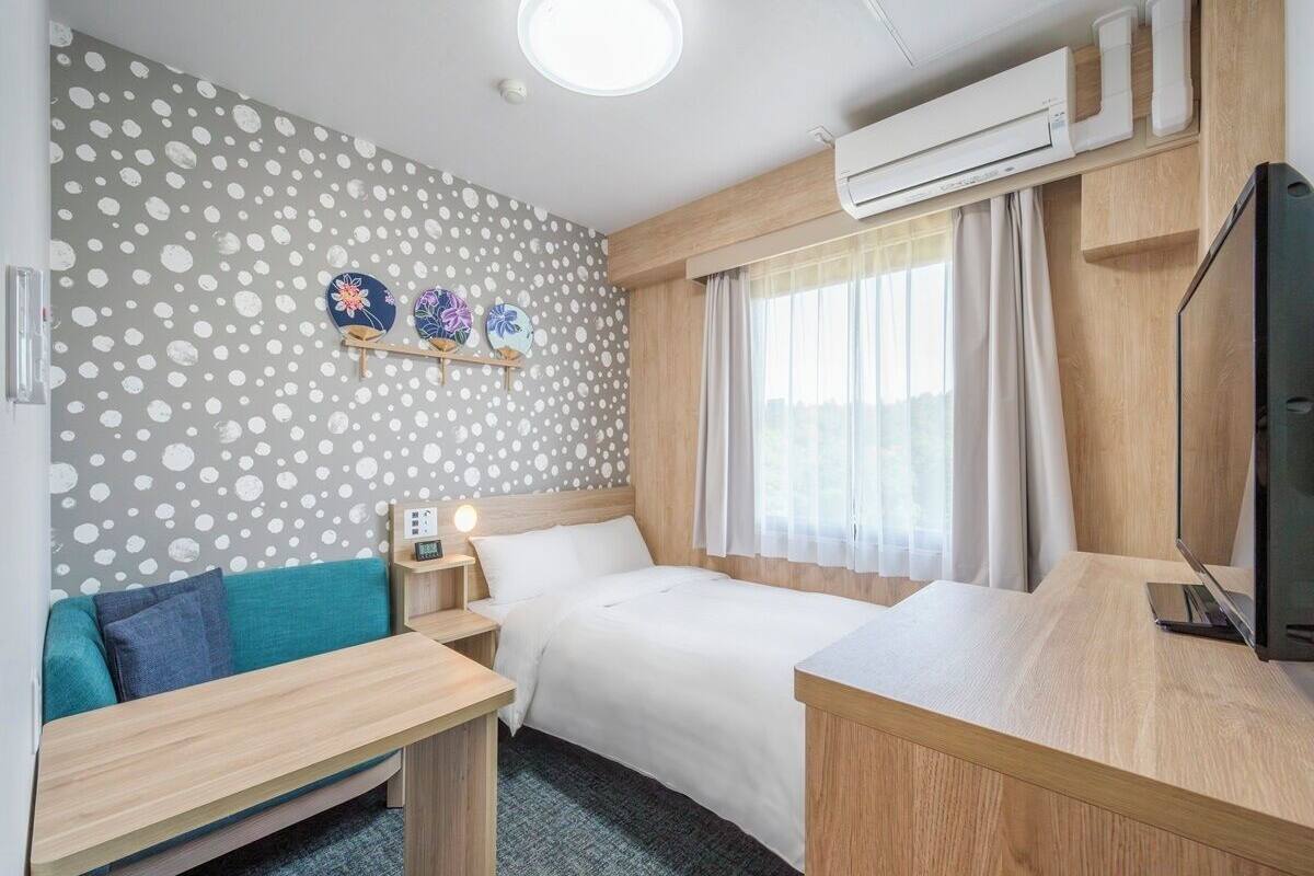 Una habitación de hotel con cama, escritorio, sofá, televisor y una pared con estampado de lunares.