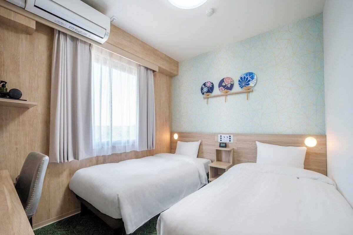 Habitación de hotel con dos camas, un escritorio, una silla y aire acondicionado instalado en la pared.