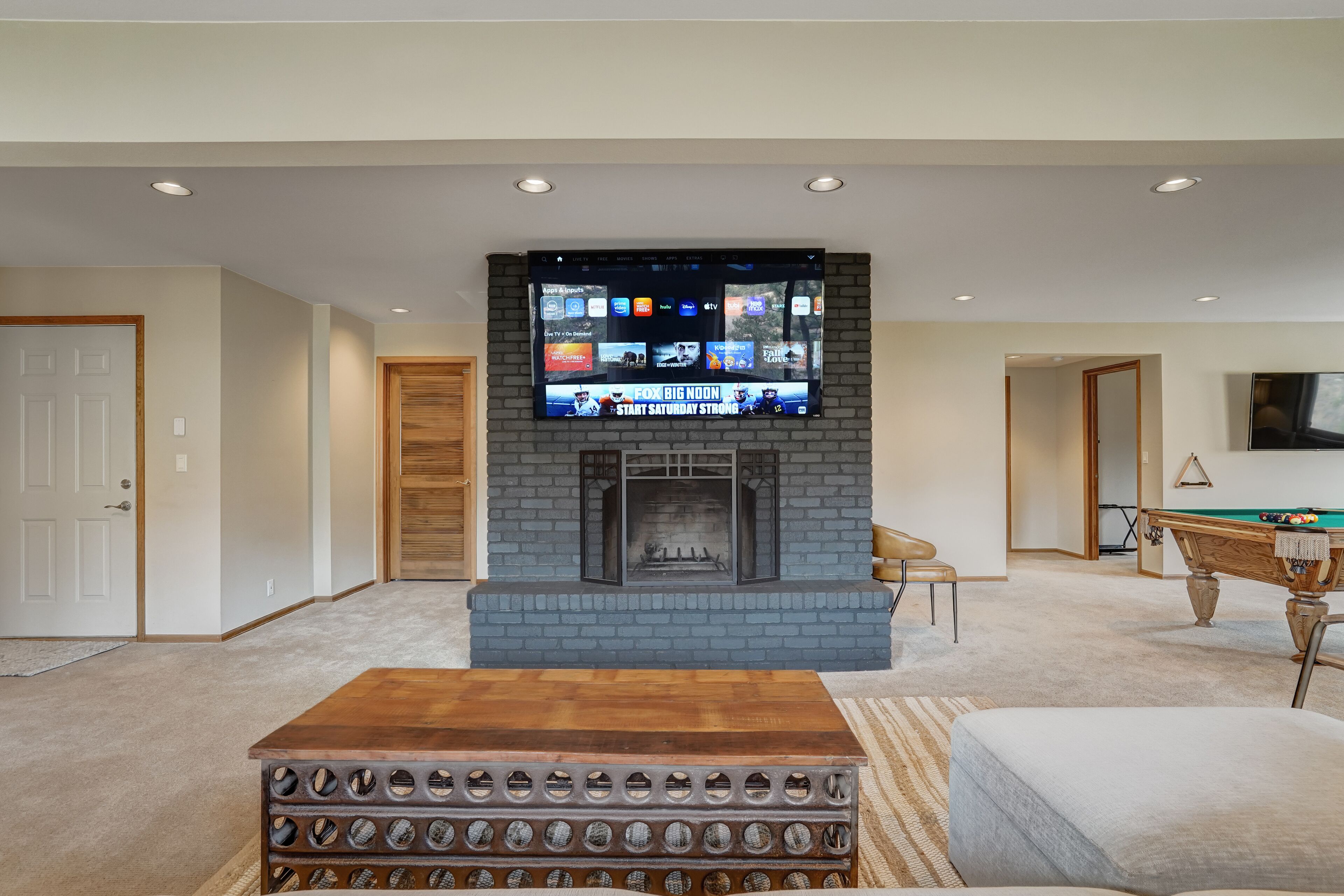A living room with a fireplace, a flat-screen TV mounted above it, and a pool table.