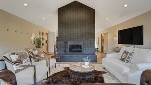 A modern living room with a fireplace, white sofas, and a large TV. - Cascadia (Cascade)
