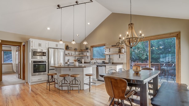 A spacious kitchen with a central island, wooden bar stools, and a dining area with a dark wooden table and chairs. - Cascadia (Cascade)