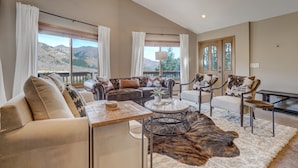 A spacious living room with a large window, a sofa set, a coffee table, and a view of the mountains. - Cascadia (Cascade)