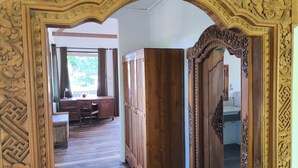 An ornate wooden doorway leading to a room with a wooden desk, chair, and a window with curtains.