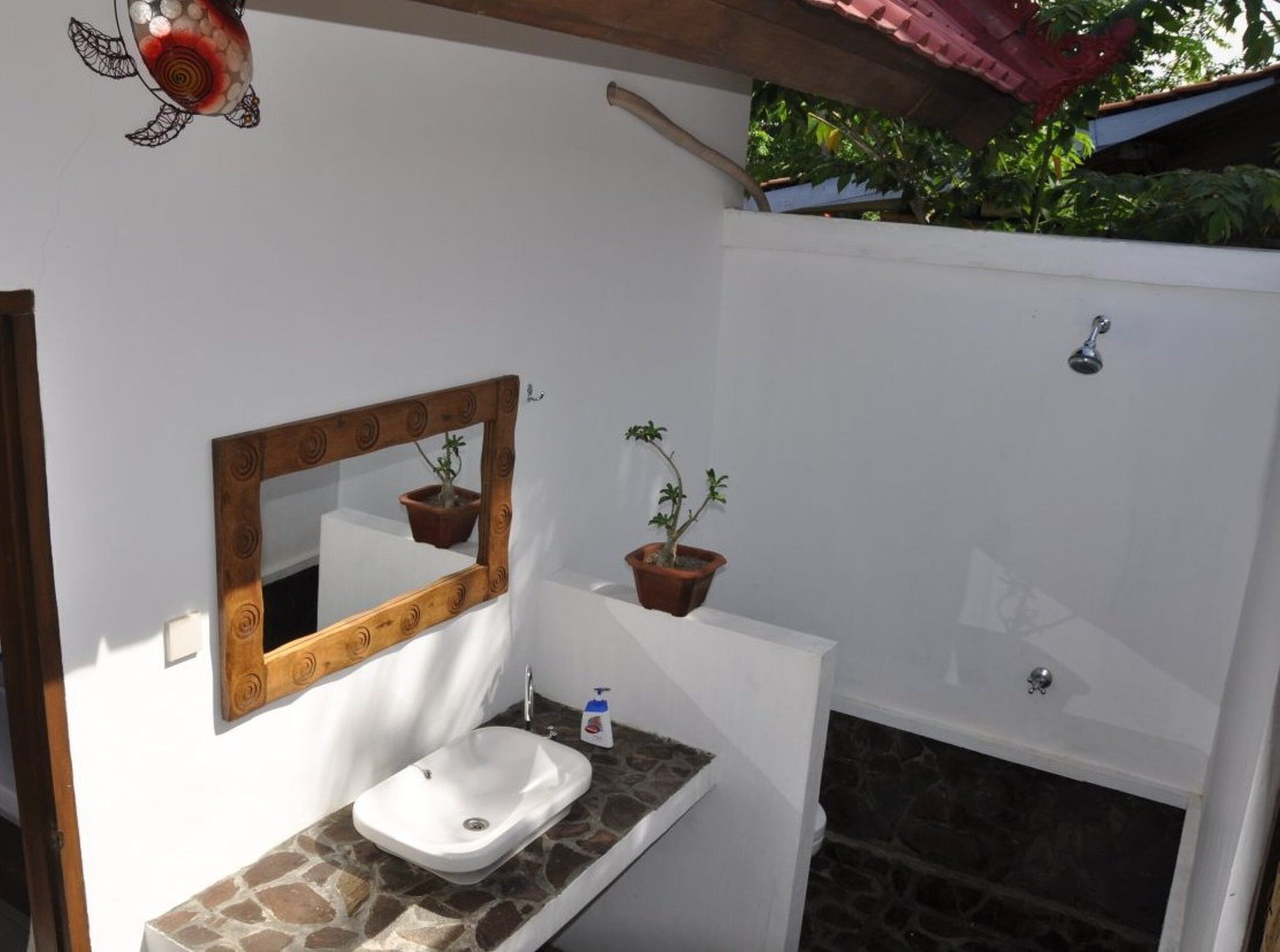 A bathroom with a white sink, a wooden-framed mirror, two potted plants, and a shower.
