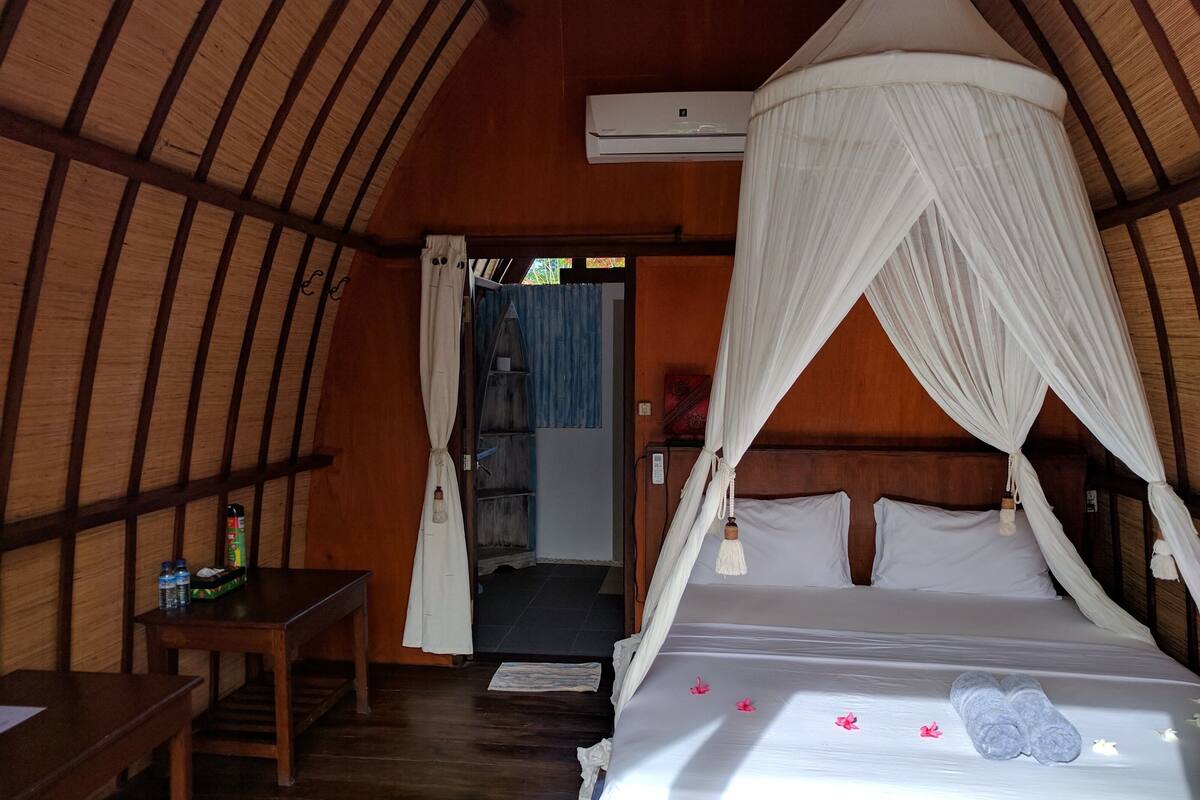 A room with a bed under a canopy, a wooden desk, and an air conditioning unit on the wall.