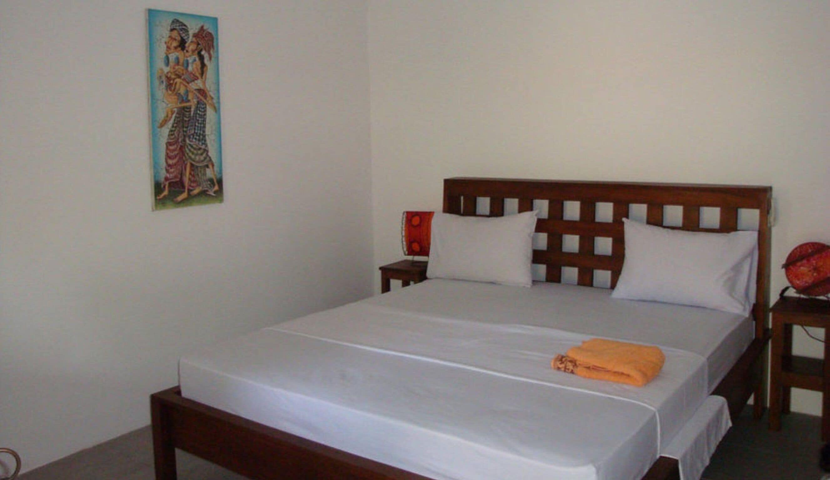 A neatly made bed with a wooden headboard, white bedding, and an orange towel.