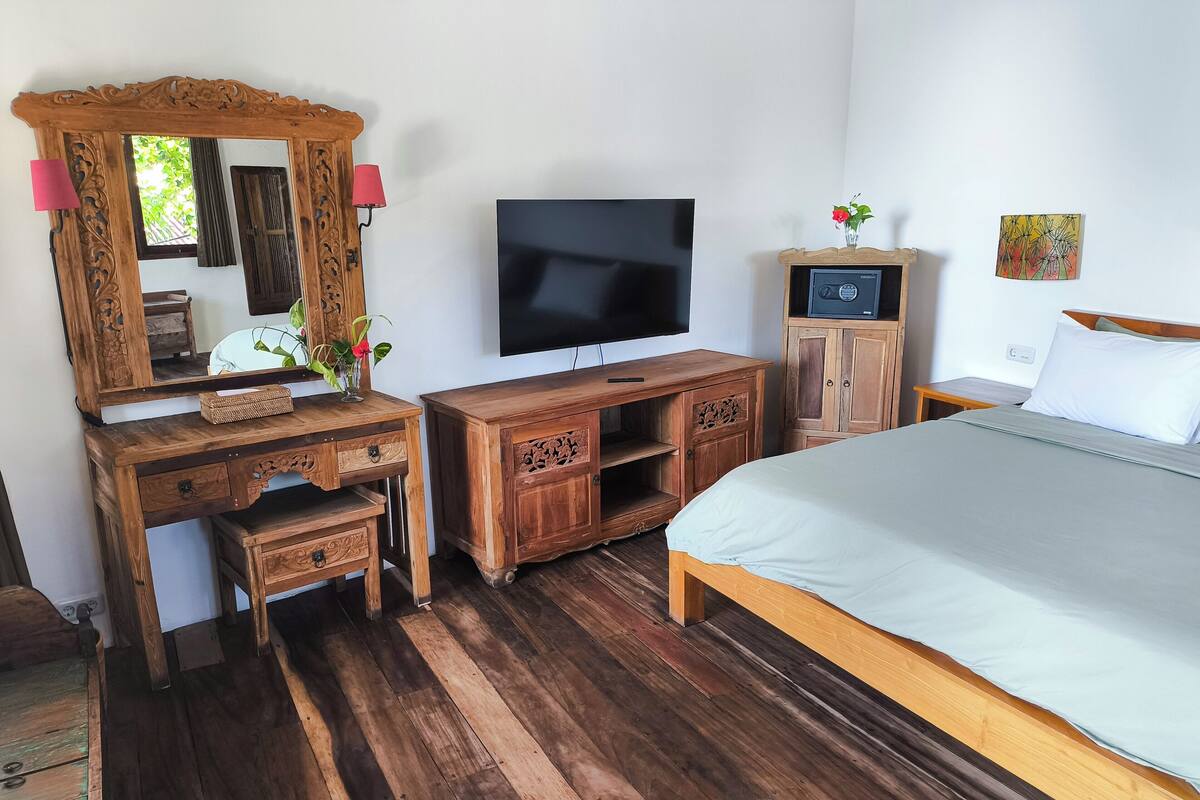 A bedroom with a wooden dresser, a TV, a cabinet, a bed, and a mirror.