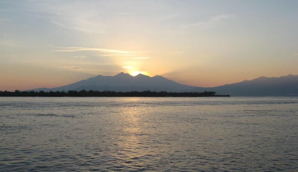 A sunset over a calm body of water with a mountain in the background.