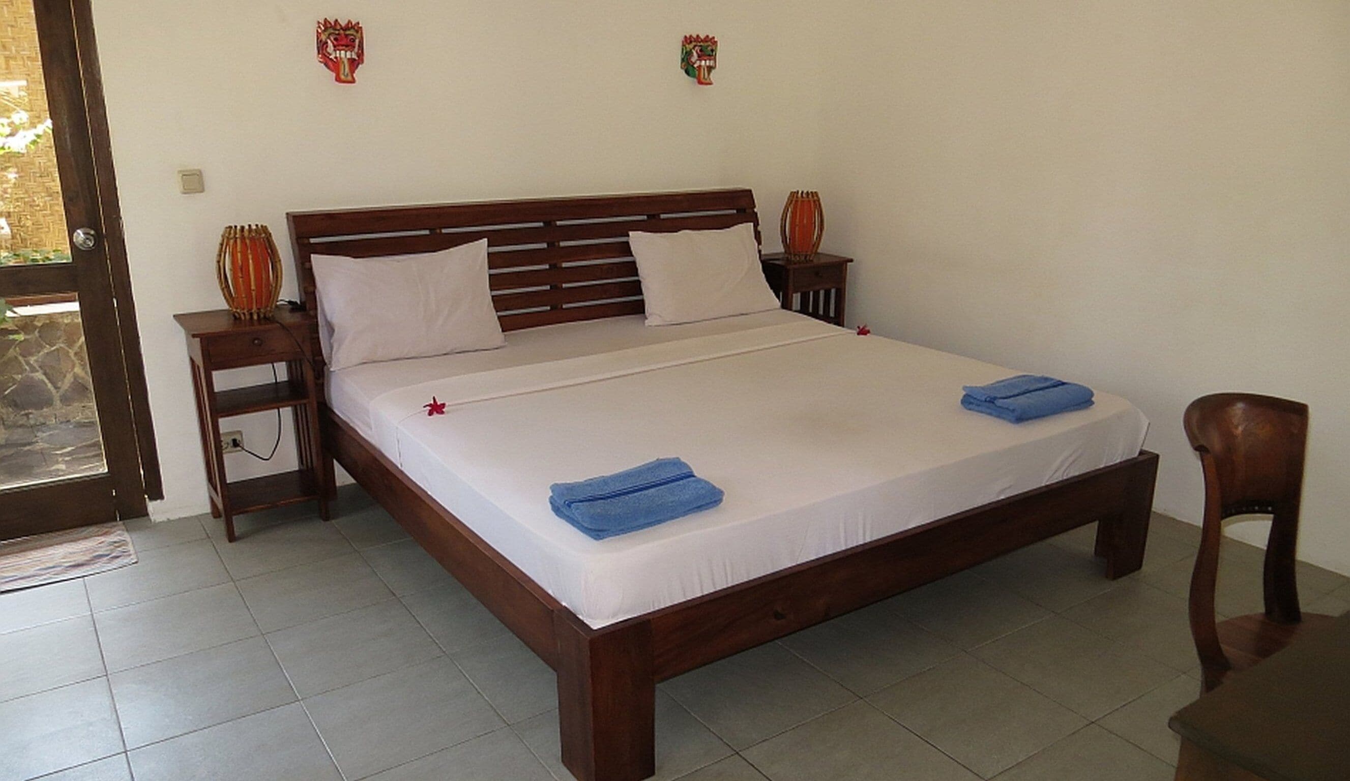 A neatly made bed with white sheets and two blue towels, a wooden headboard, and two decorative wall pieces.