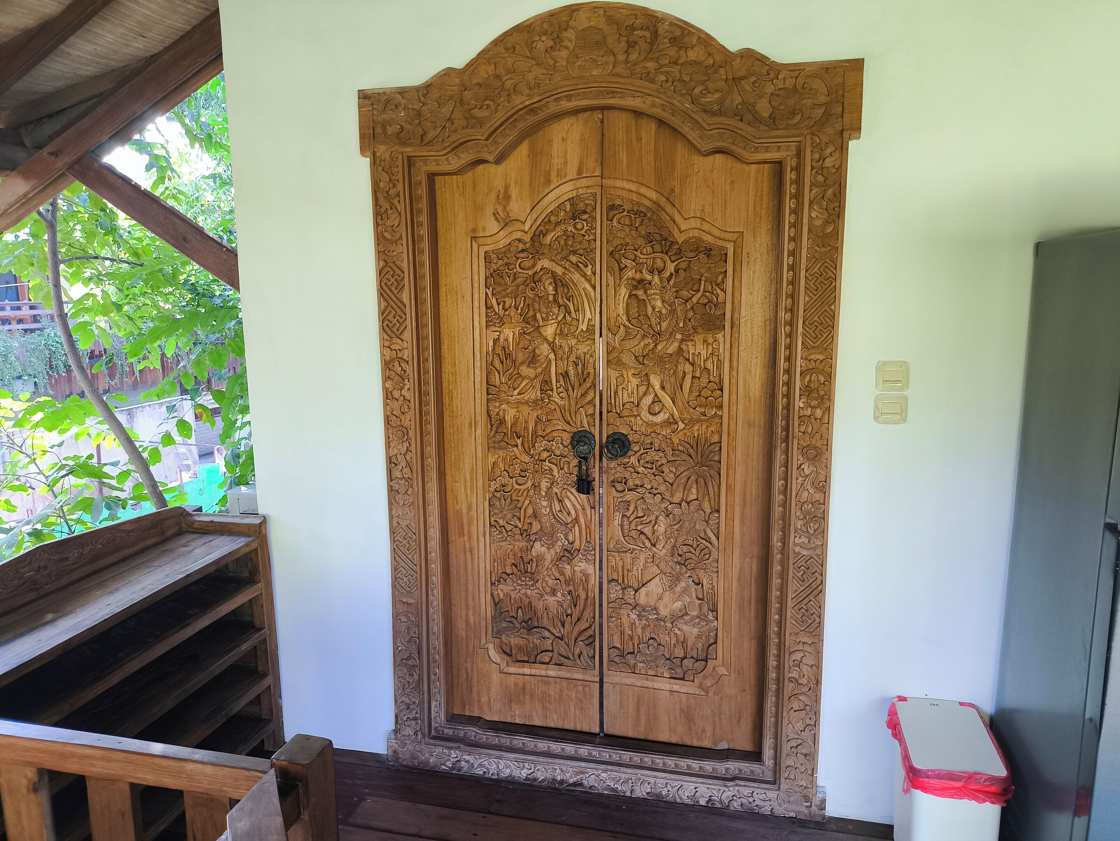 A wooden door with intricate carvings, a bench, and a trash bin.