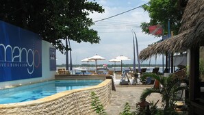 A pool area with a stone wall, umbrellas, and a view of the sea.