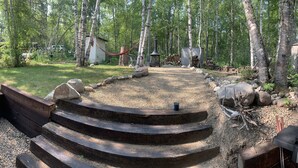 A backyard with a wooden staircase leading to a gravel area, surrounded by trees and a barbecue grill. - 4 Season Cabin great for Summer or Winter activities! 
Excellent Green Space (Marean Lake)