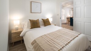 Une chambre à coucher avec un lit, des lampes de chevet, un tableau encadré et une porte donnant sur une autre pièce.