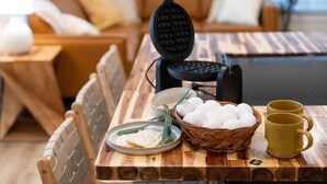 Une table de salle à manger en bois, avec un gaufrier, des œufs, un sachet de thé et deux tasses.