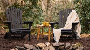 Deux fauteuils Adirondack, une couverture et une petite table sur laquelle se trouve une tasse jaune, le tout dans un décor forestier.