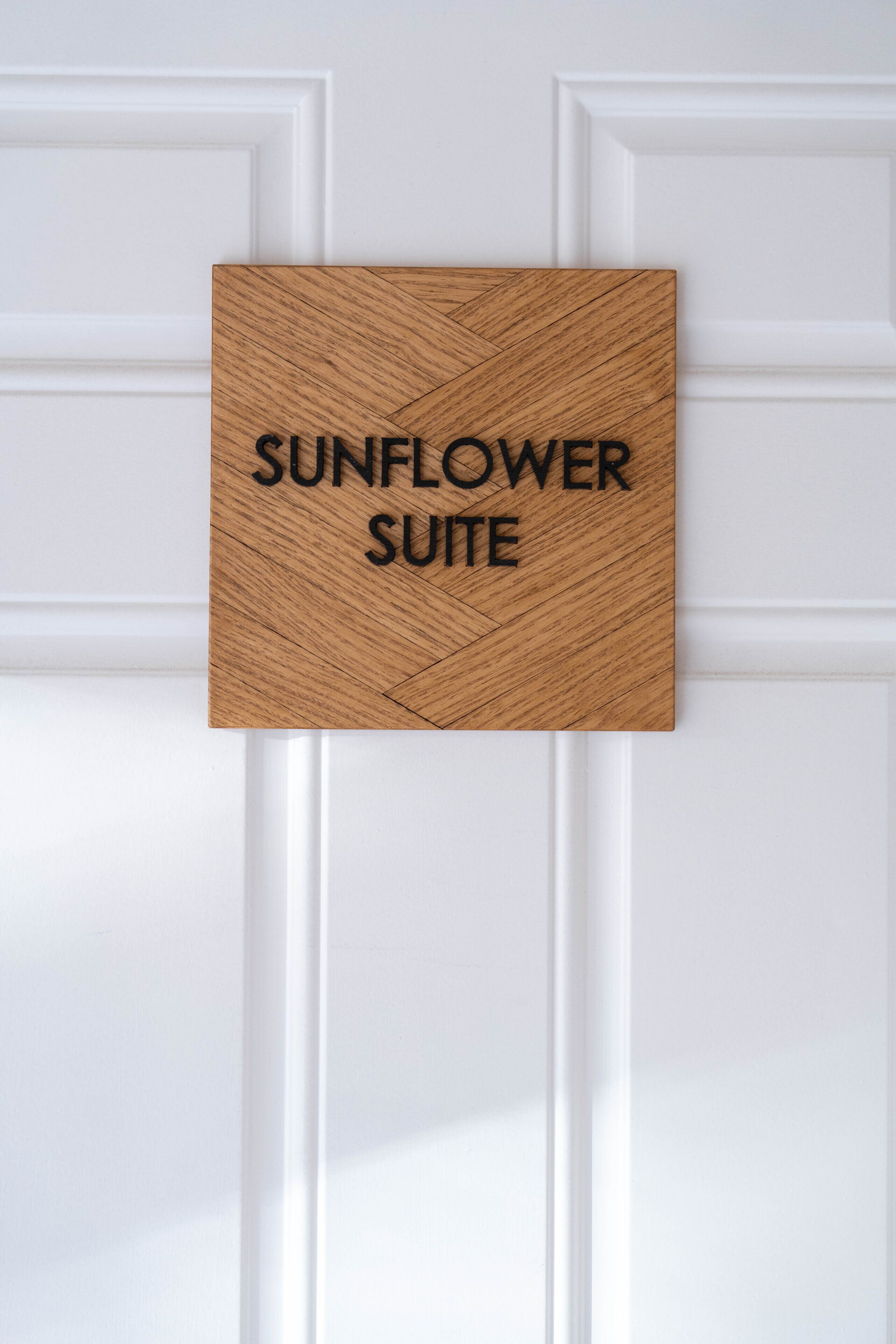 Un letrero de madera con el texto "SUNFLOWER SUITE" colocado en una puerta blanca.